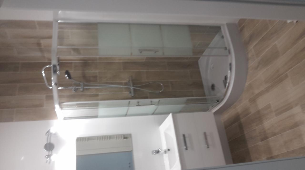 Wykończona łazienka z kabiną prysznicową z półokrągłą szybą, umywalką z szafką i brązowymi płytkami imitującymi drewno na ścianach.