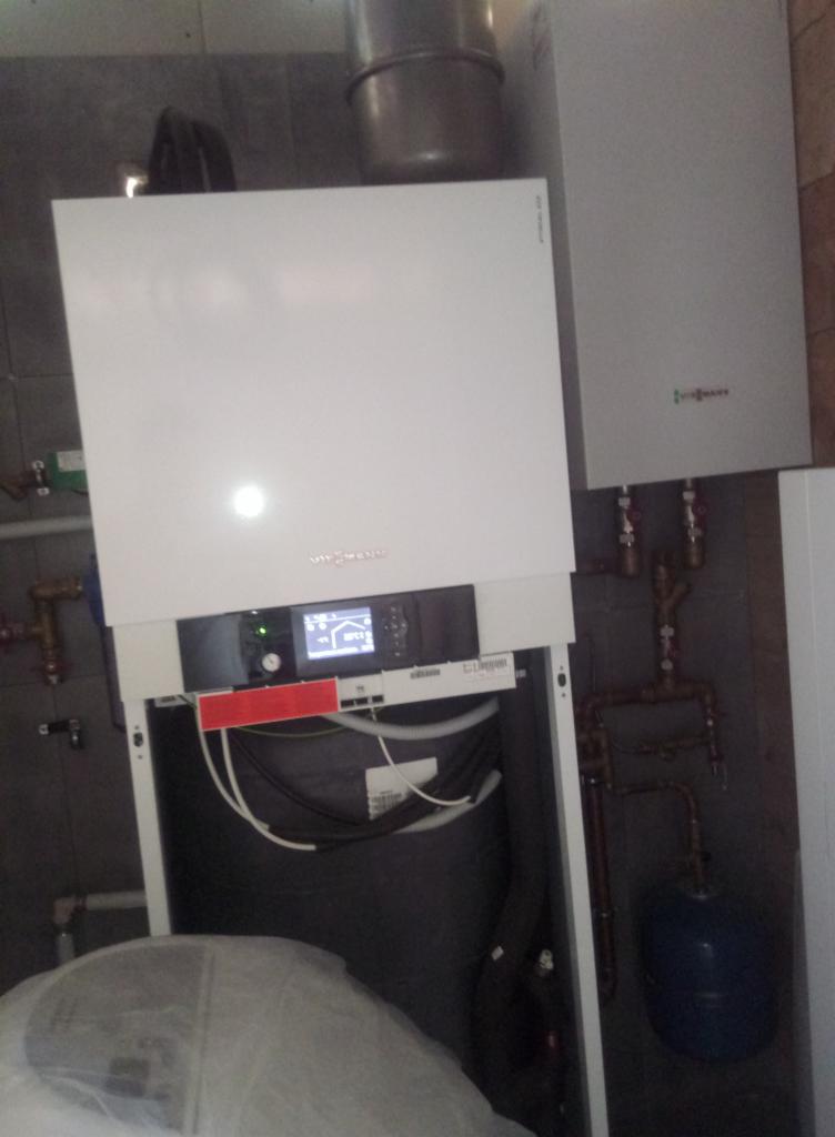 Biały piec grzewczy Viessmann z podłączonymi rurami miedzianymi i niebieskim zbiornikiem wyrównawczym, widoczne elementy instalacji centralnego ogrzewania.