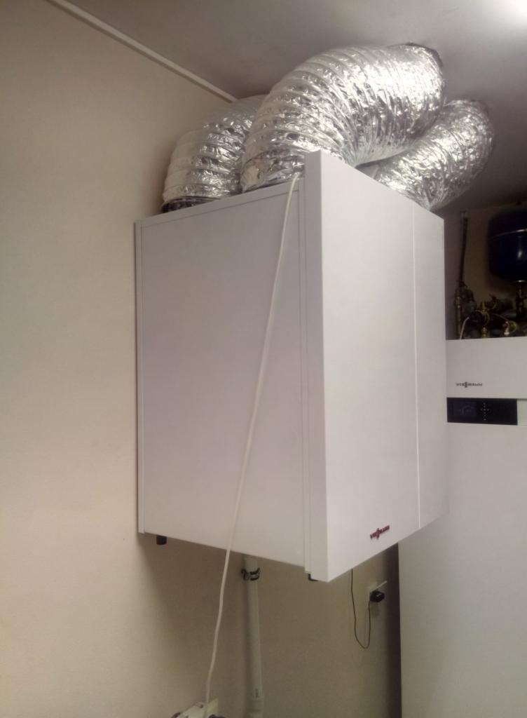 Biały piec gazowy Viessmann z podłączonymi aluminiowymi przewodami wentylacyjnymi, zamontowany na ścianie w pomieszczeniu.