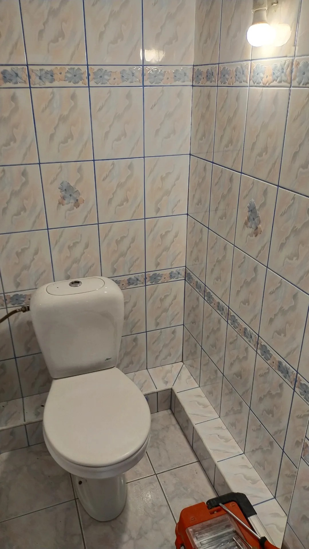 Ukończona toaleta w łazience w Pewel Ślemieńska, z beżowymi płytkami z kwiatowym wzorem i widoczną skrzynką z narzędziami na podłodze.