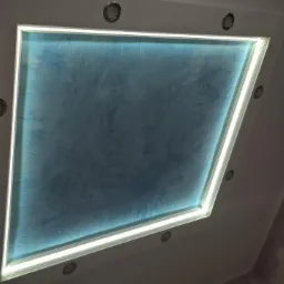 Nietypowy sufit podwieszany z oświetleniem LED i dekoracyjną, niebieską fakturą przypominającą chmury, uzupełniony punktowymi lampami halogenowymi.