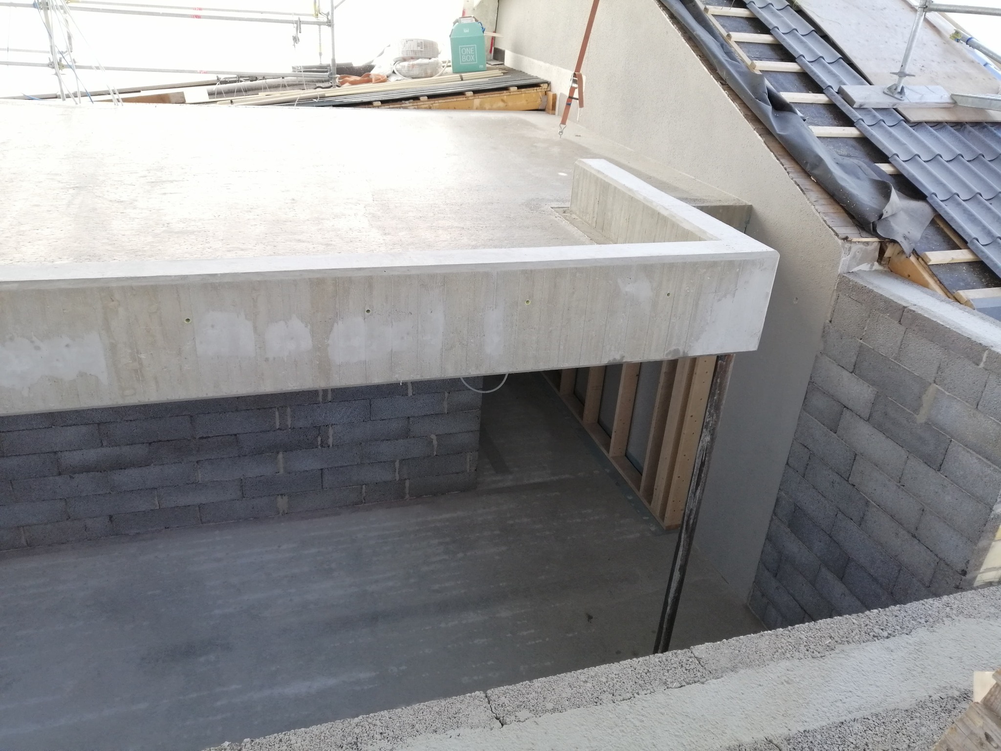 Surowy stan domu murowanego w trakcie budowy: ściany z szarego bloczka, wylewka betonowa, widoczne elementy konstrukcji dachu i rusztowania.