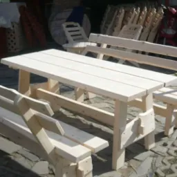 Surowe drewniane meble ogrodowe: stół z dwiema ławkami z oparciami w niezagospodarowanym otoczeniu.