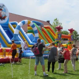 Kolorowy park dmuchany z motywem pirackim na trawniku, otoczony grupą dzieci i dorosłych w słoneczny dzień.