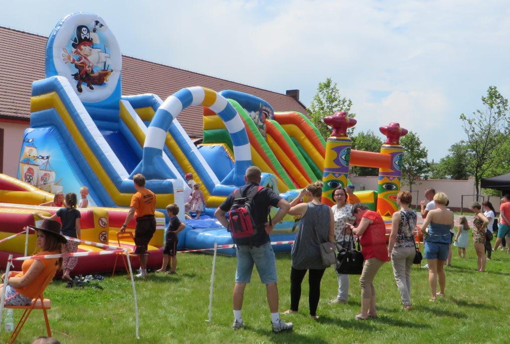 Kolorowy park dmuchany z motywem pirackim na trawniku, otoczony grupą dzieci i dorosłych w słoneczny dzień.