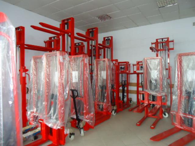 Magazyn z nowymi, czerwonymi wózkami paletowymi, niektóre owinięte w folię ochronną, ustawione w rzędach w jasnym pomieszczeniu.