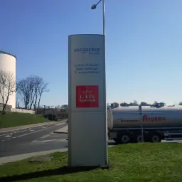 Pylon informacyjny z logo Südzucker Polska i Cukier Królewski na tle zbiornika przemysłowego i cysterny Angama, błękitne niebo.