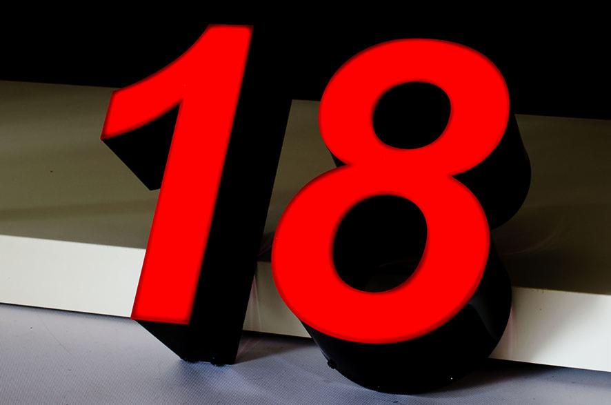 Podświetlane, trójwymiarowe cyfry '18' w kolorze czerwonym z czarnymi bokami, ustawione na jasnej powierzchni, z ciemnym tłem.