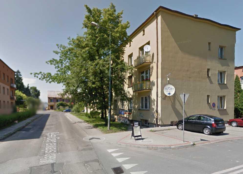 Budynek mieszkalny z anteną satelitarną na balkonie i okrągłym szyldem reklamowym na ścianie, widok z ulicy.