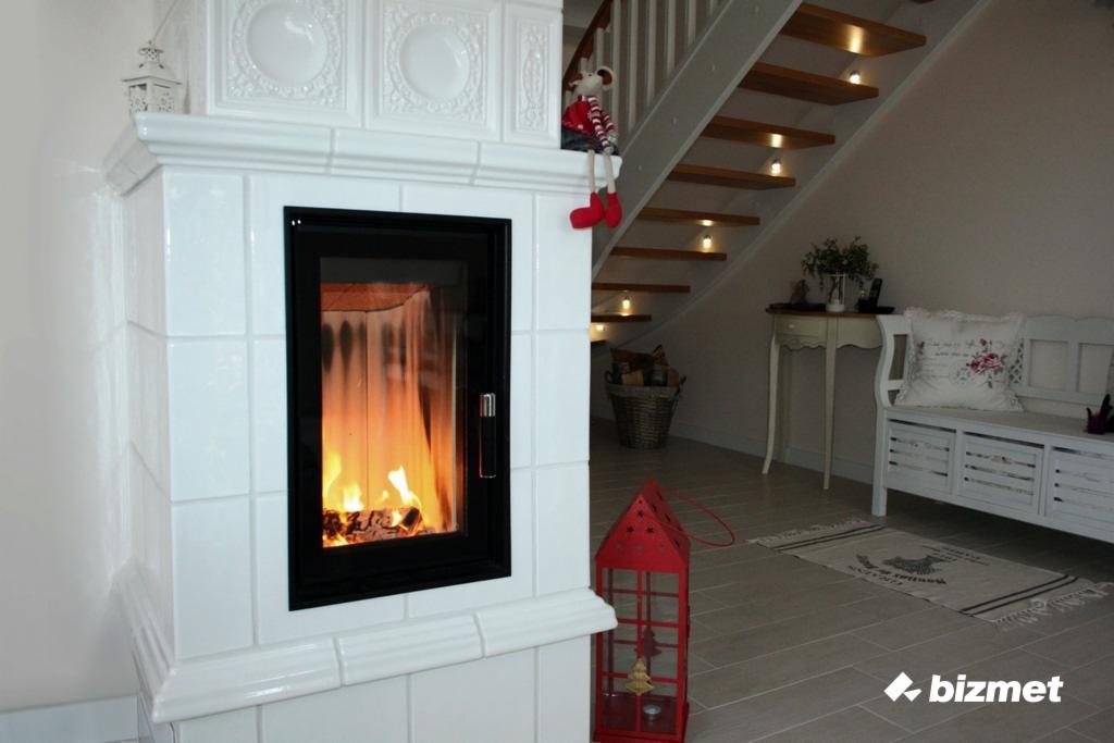 Nowoczesny kominek kaflowy z czarnym obramowaniem w Złotowie, z palącym się ogniem i ozdobną figurką myszki siedzącą na górze, w tle schody z oświetleniem punktowym.