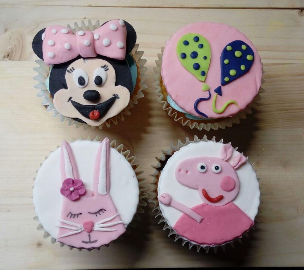 Cztery dekorowane babeczki na drewnianym stole: jedna z Minnie Mouse z różową kokardą w kropki, druga z dwoma balonami, trzecia z różowym zajączkiem z kwiatkiem, czwarta z świnką Peppą.
