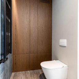 FURSTA Meble Wojciech Ziembla - Nowoczesna łazienka z drewnianą szafą wnękową, grzejnikiem drabinkowym i podwieszaną toaletą. Minimalistyczny design, płytki imitujące kamień.