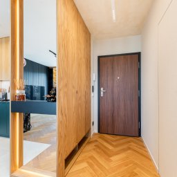 FURSTA Meble Wojciech Ziembla - Nowoczesny przedpokój z drewnianą szafą wnękową i lustrem z podświetleniem LED. Parkiet ułożony w jodełkę. Widok na kuchnię z zielonymi szafkami.