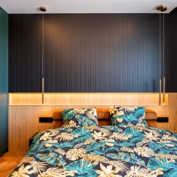 FURSTA Meble Wojciech Ziembla - Nowoczesna sypialnia z turkusową szafą, panelem ściennym w kolorze antracytu i drewnianym wezgłowiem z oświetleniem LED. Pościel w tropikalne liście.