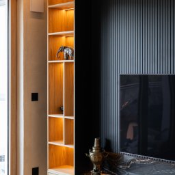 FURSTA Meble Wojciech Ziembla - Nowoczesna szafka RTV z podświetleniem LED i otwartym regałem, dekorowana figurką słonia i samowarem. Czarny panel ścienny z pionowymi listwami. Jasne drewno i marmur.