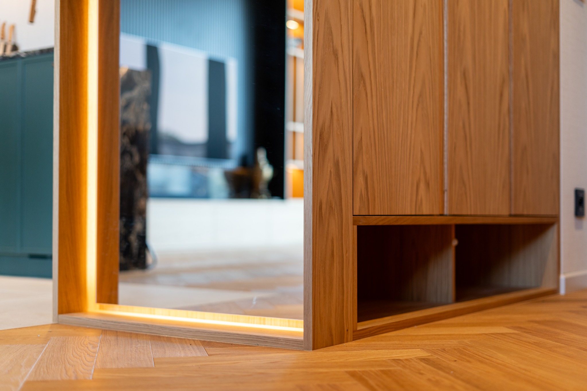 Drewniana szafa z oświetleniem LED, widoczna z perspektywy podłogi. Parkiet w jodełkę, odbicie w lustrze. Nowoczesny design, ciepłe światło.