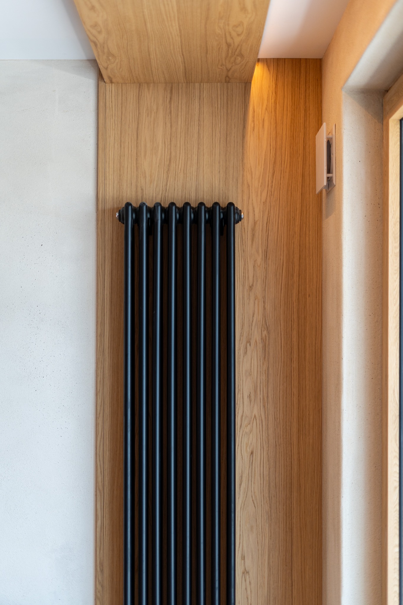 Czarny, żeliwny grzejnik dekoracyjny na tle drewnianej boazerii i jasnej ściany. Minimalistyczny design, ciepłe oświetlenie, nowoczesne wnętrze.