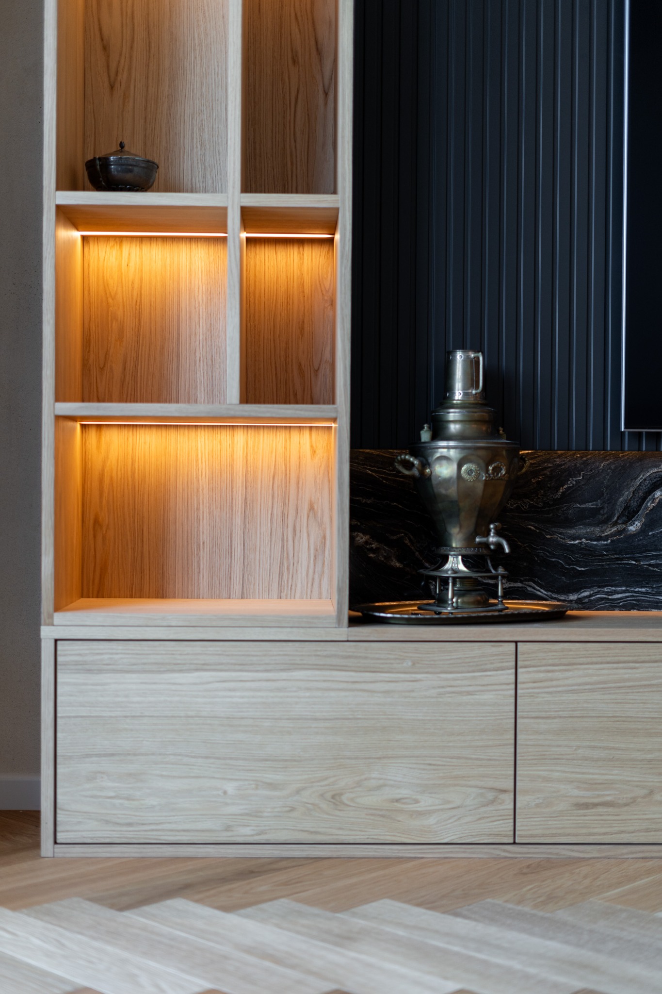 Drewniana szafka z oświetleniem LED i dekoracyjnym samowarem na blacie z czarnego marmuru. Parkiet w jodełkę na podłodze. Nowoczesny design.