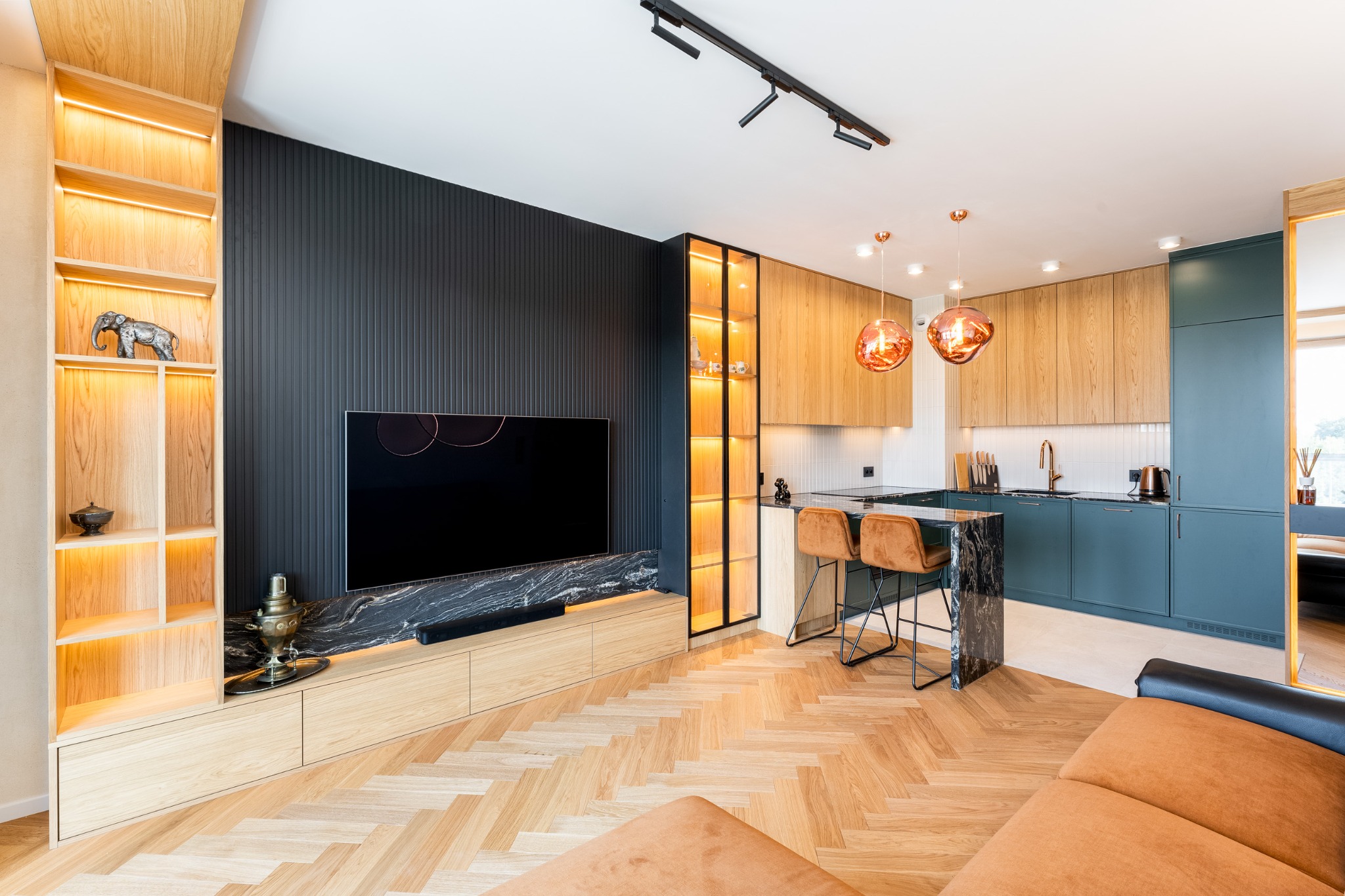 Nowoczesna aranżacja wnętrza: drewniana zabudowa TV z marmurowym blatem, podświetlana witryna i kuchnia z zielonymi szafkami oraz wyspą z hokerami.