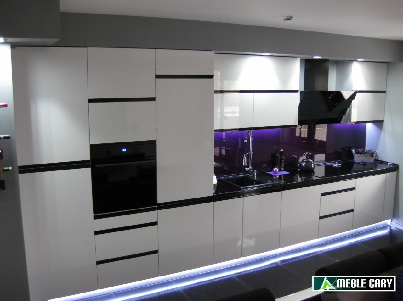 Nowoczesna kuchnia z białymi, lakierowanymi frontami szafek, czarnym blatem i fioletowym podświetleniem ściany nad blatem, dodatkowo podświetlenie LED u dołu szafek.