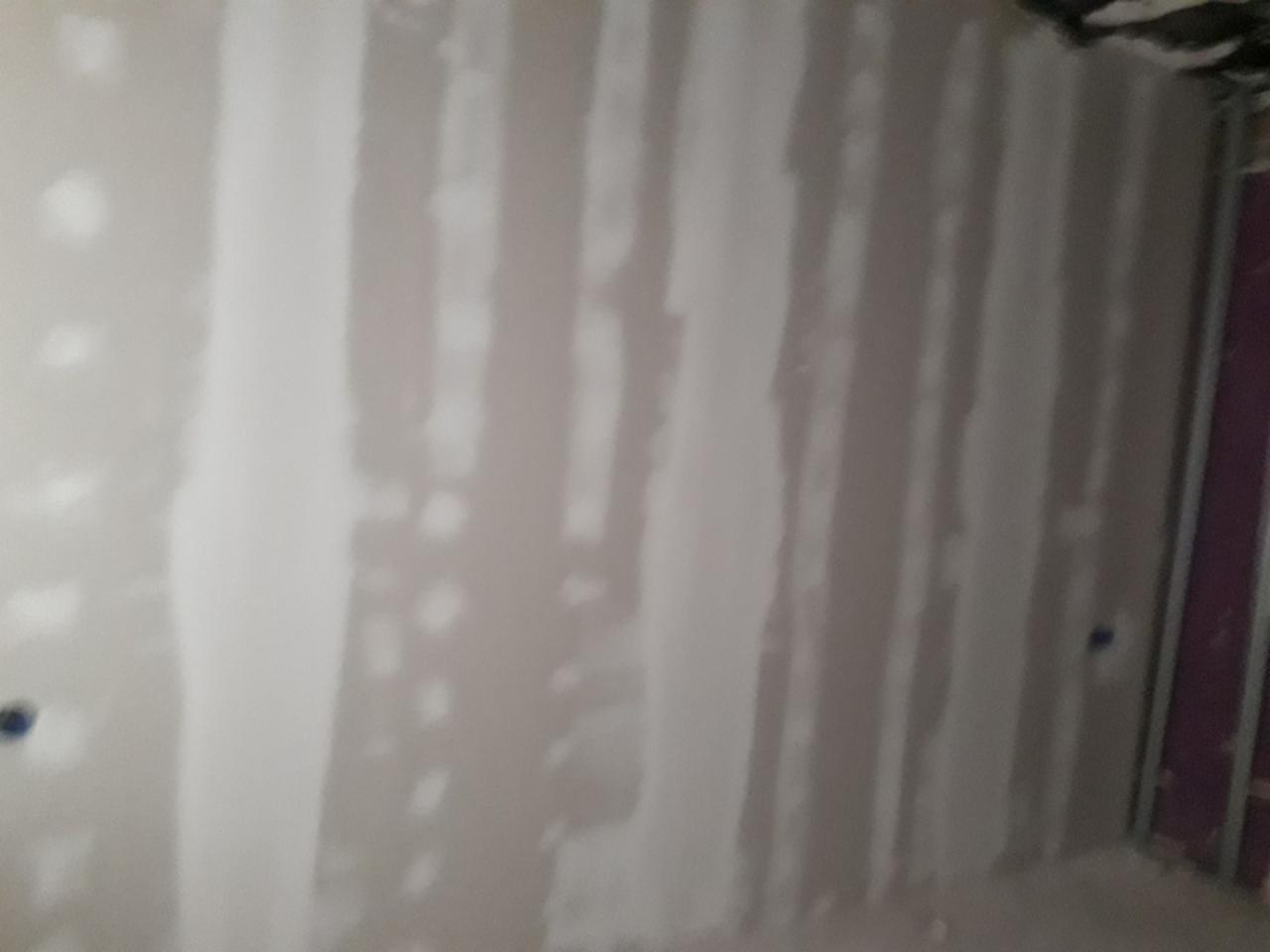 Ściana w trakcie szpachlowania łączeń płyt gipsowo-kartonowych, widoczne metalowe profile konstrukcyjne.