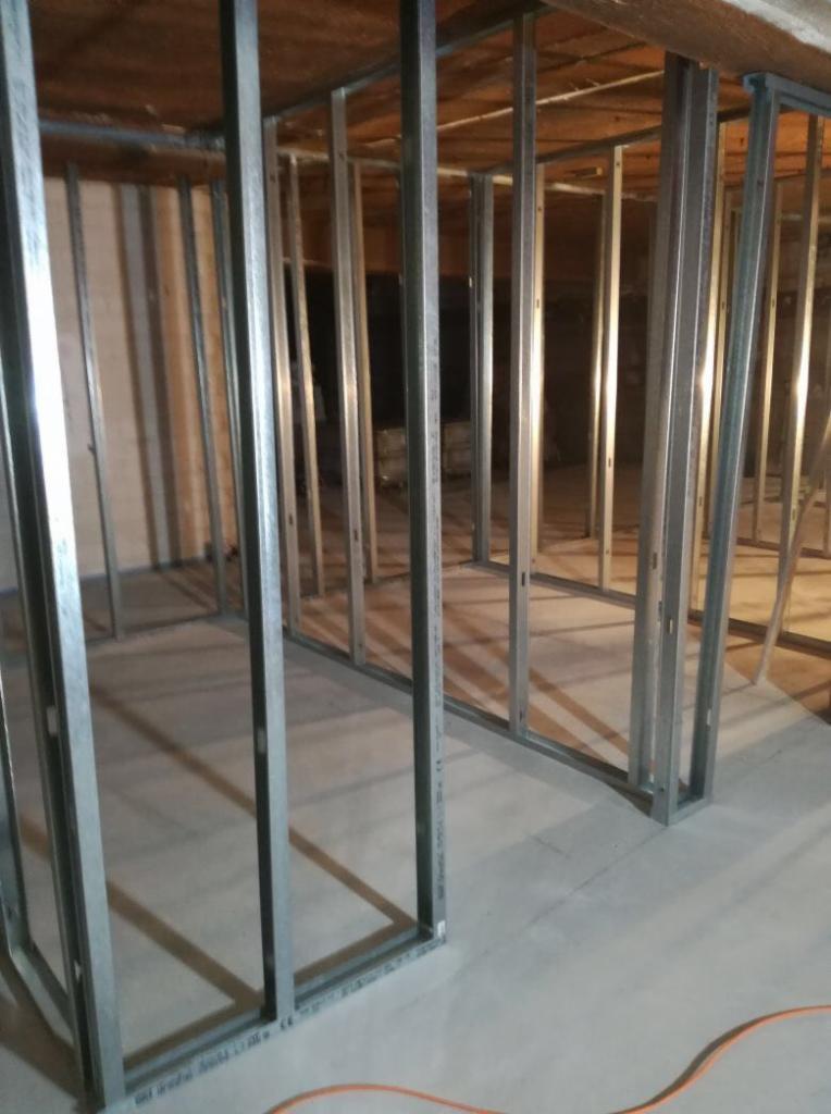 Metalowa konstrukcja szkieletowa ścian działowych w surowym stanie, widoczne profile stalowe na betonowej podłodze, przygotowanie do montażu okładzin.