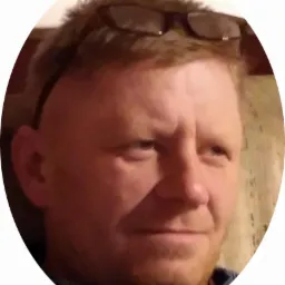 Portret mężczyzny z okularami na głowie, uśmiechającego się lekko w kierunku prawego g&oacute;rnego rogu kadru.