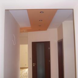 Ireneusz Osiecki - Korytarz po remoncie z pomalowanym sufitem na pomarańczowo z wbudowanymi halogenami oraz dwiema ciemnymi drewnianymi drzwiami po prawej stronie.