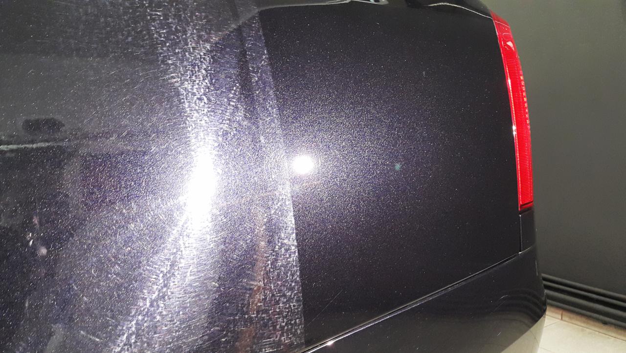 Część karoserii ciemnego samochodu przed i po polerowaniu, widoczne liczne zarysowania po lewej stronie i gładka powierzchnia po prawej.