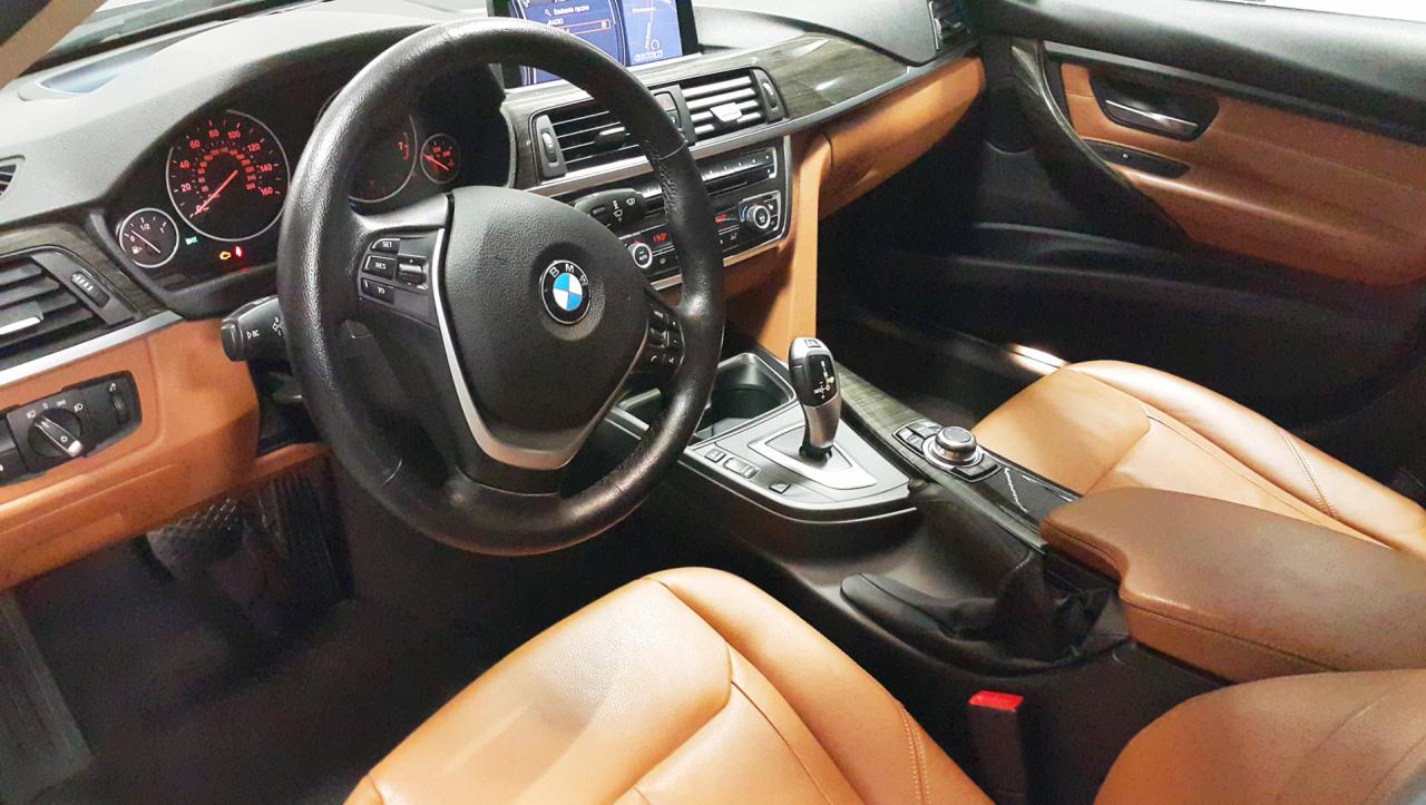 Wnętrze samochodu BMW z brązową skórzaną tapicerką, widok na deskę rozdzielczą, kierownicę i dźwignię zmiany biegów.