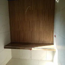 Wnęka prysznicowa wyłożona płytkami imitującymi drewno, z półką z tego samego materiału, białe marmurowe płytki na ścianach, sufit w trakcie malowania, widoczne krzyżyki glazurnicze.