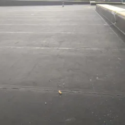 Płaski dach pokryty czarną membraną bitumiczną, widoczne łączenia pasów, fragment obróbki krawędziowej z płyt OSB.