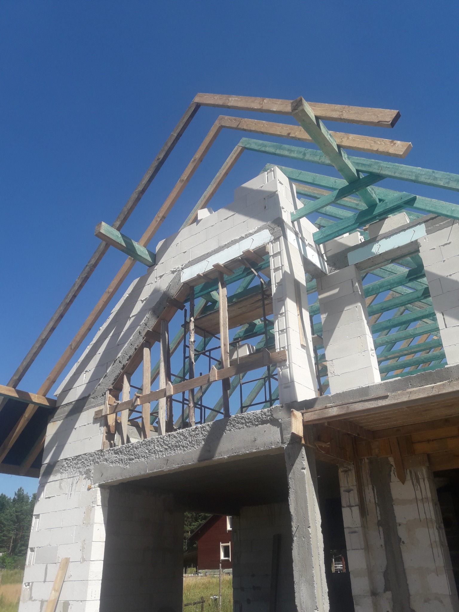 Budowa domu z białych bloczków, widoczne drewniane elementy konstrukcji dachu i stropu, błękitne niebo w tle.