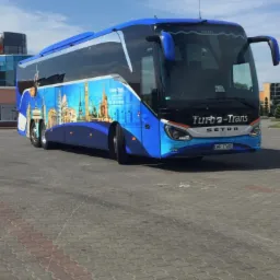 Niebieski autokar Setra Turbo-Trans z panoramą europejskich miast na boku, zaparkowany na placu z kostki brukowej.