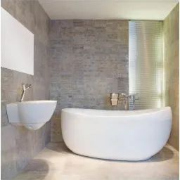 Nowoczesna łazienka z owalną wanną, wiszącą umywalką i szarą okładziną ścienną imitującą kamień, oświetlona przez pionowe żaluzje okienne.