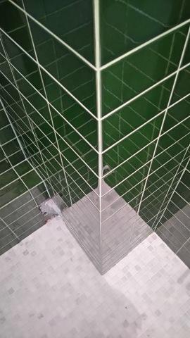 Wysoki kąt widzenia na narożnik wyłożony zielonymi, kwadratowymi płytkami z białymi fugami, przechodzący w szarą, mozaikową podłogę.