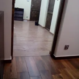 Ułożone ciemne panele podłogowe w korytarzu, widoczne przejście między dwoma rodzajami paneli, w tle drzwi z ciemnego drewna.