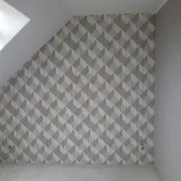 Ściana w pokoju na poddaszu pokryta tapetą z geometrycznym wzorem w odcieniach szarości, beżu i bieli. Widoczne gniazdka elektryczne na ścianie.