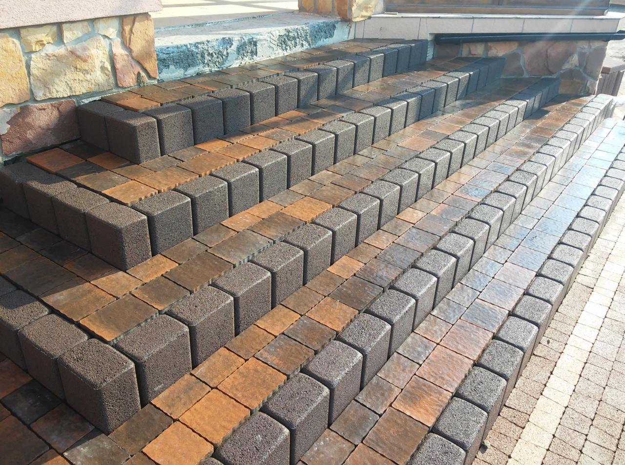 Schody wejściowe wyłożone kostką brukową w odcieniach brązu i grafitu, widok z góry ukazujący regularny wzór ułożenia kostki.