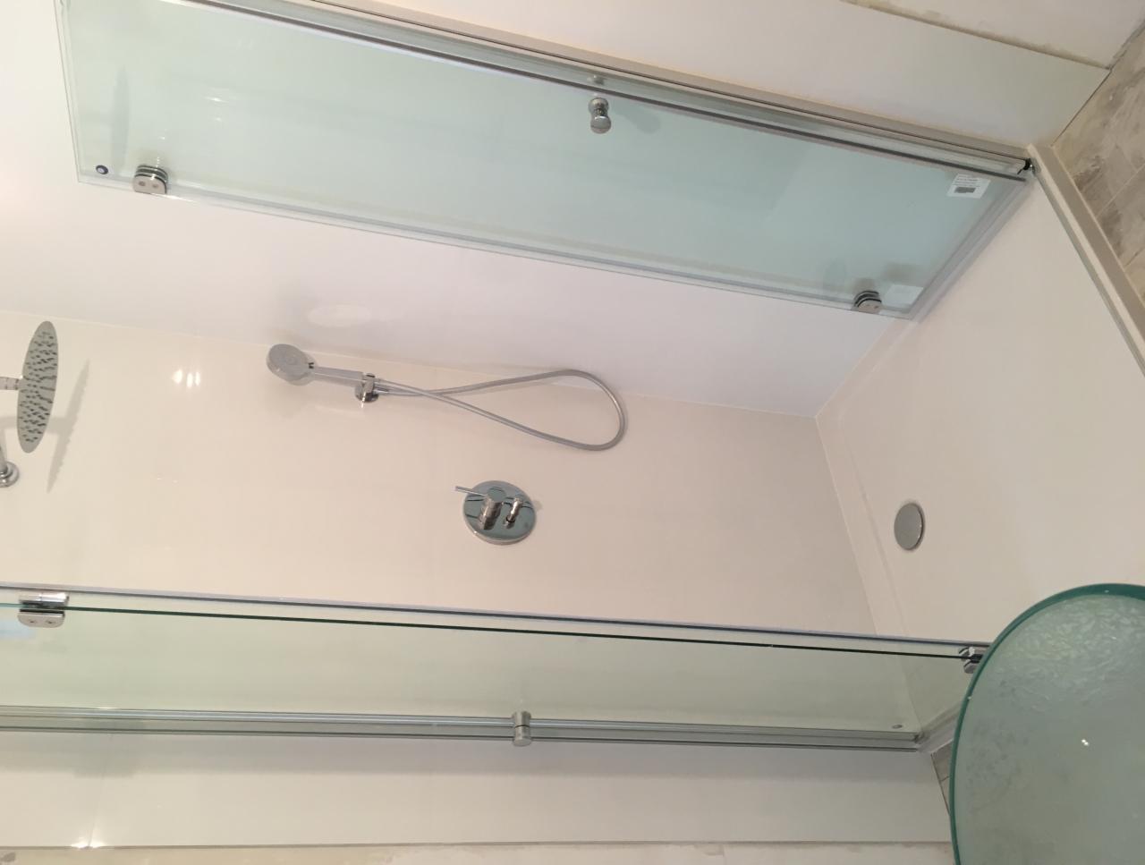 Szklana kabina prysznicowa z przesuwnymi drzwiami, widok od dołu, z zamontowaną deszczownicą i słuchawką prysznicową oraz baterią.