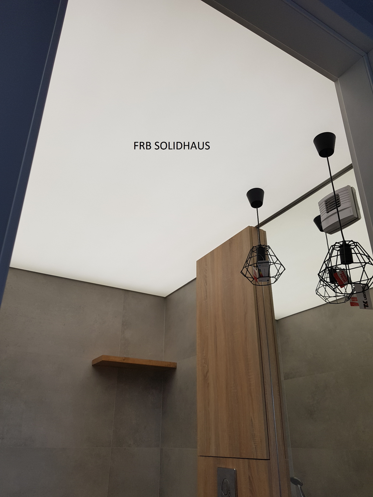 Nowoczesna łazienka z szarą glazurą, drewnianą szafką, podświetlanym sufitem i minimalistycznymi lampami wiszącymi w metalowych kloszach.