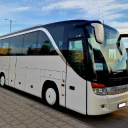 Biały autokar Setra S 411 HD zaparkowany na chodniku z kostki, z widocznym logo firmy Wilson na przedniej szybie, odbijający budynki w oknach.