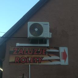ArkonTech Paulina Kędzia - Zewnętrzna jednostka klimatyzacji marki Kaisai zamontowana na brązowej ścianie budynku nad banerem reklamowym z napisem 'Żaluzje Rolety' i czerwoną strzałką.