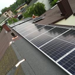 ArkonTech Paulina Kędzia - Montaż paneli fotowoltaicznych na dachu domu jednorodzinnego, widoczny instalator w czapce, pochmurne niebo.