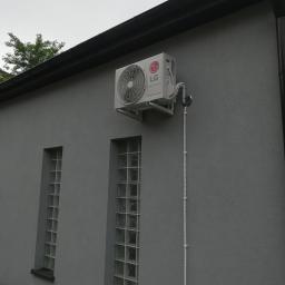 ArkonTech Paulina Kędzia - Zewnętrzna jednostka klimatyzacji LG zamontowana na szarej ścianie budynku z dwoma oknami z luksferami, widoczne elementy instalacji.