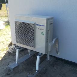 ArkonTech Paulina Kędzia - Zewnętrzna jednostka klimatyzacji Panasonic Inverter R32 zamontowana na metalowym stelażu przy ścianie budynku, z widocznymi przewodami i pianką uszczelniającą.