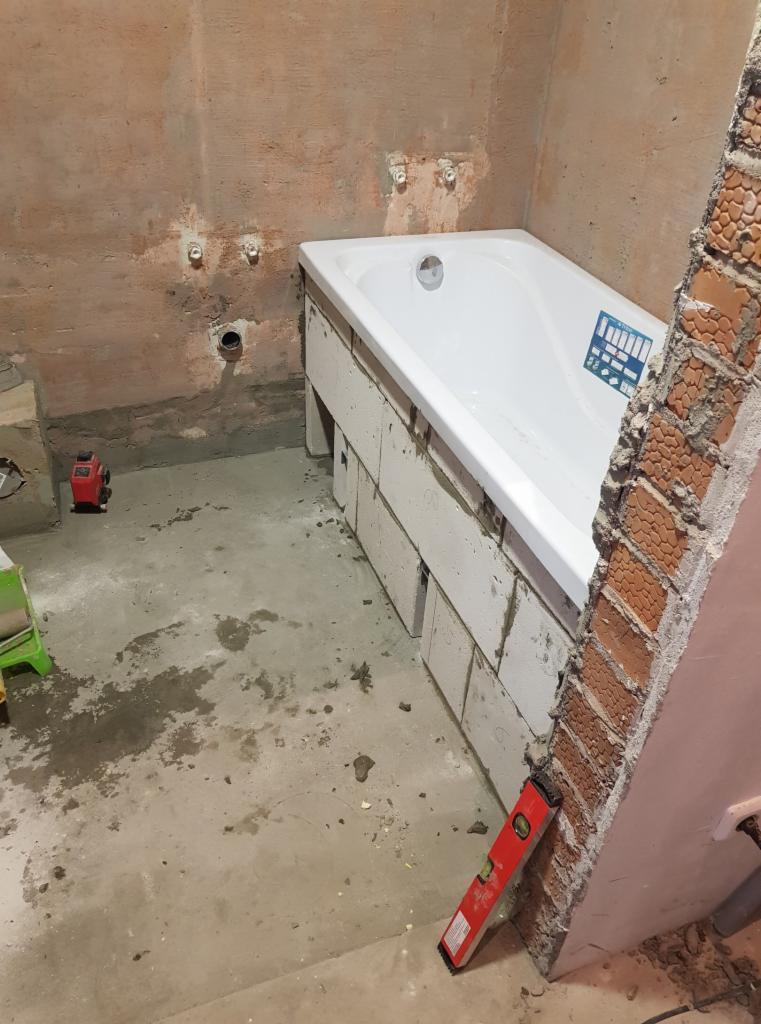 Montaż wanny: biała wanna obudowana bloczkami, widoczna poziomica, laser krzyżowy i surowa ściana z instalacją hydrauliczną w trakcie prac wykończeniowych.
