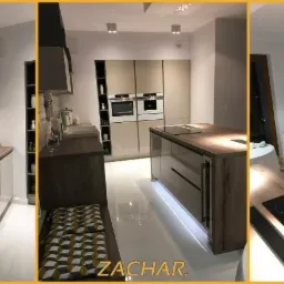 Nowoczesna kuchnia z wyspą, jasne fronty szafek, drewniane blaty, białe płytki na ścianie, oświetlenie podszafkowe, widoczne AGD w zabudowie.