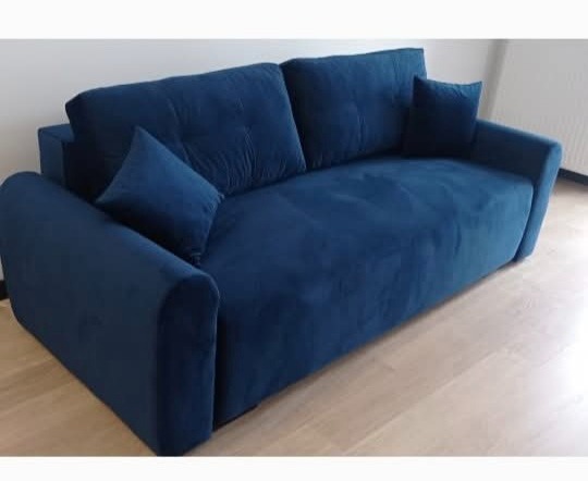 Granatowa, welurowa sofa z poduszkami w minimalistycznym wnętrzu. Nowoczesny design, komfortowe siedzisko, idealna do salonu. Tapicerka wysokiej jakości.