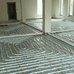 Rozłożone rury ogrzewania podłogowego na izolacji, przed wylaniem posadzki w przestronnym, jasnym pomieszczeniu z kolumną.